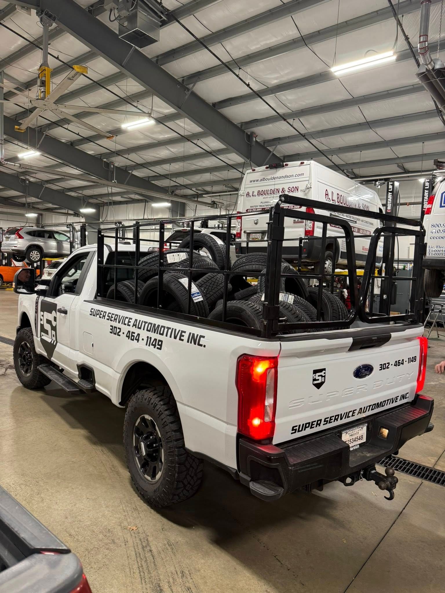 White off-road utility pickup with roll cage and spare tires inside a warehouse garage