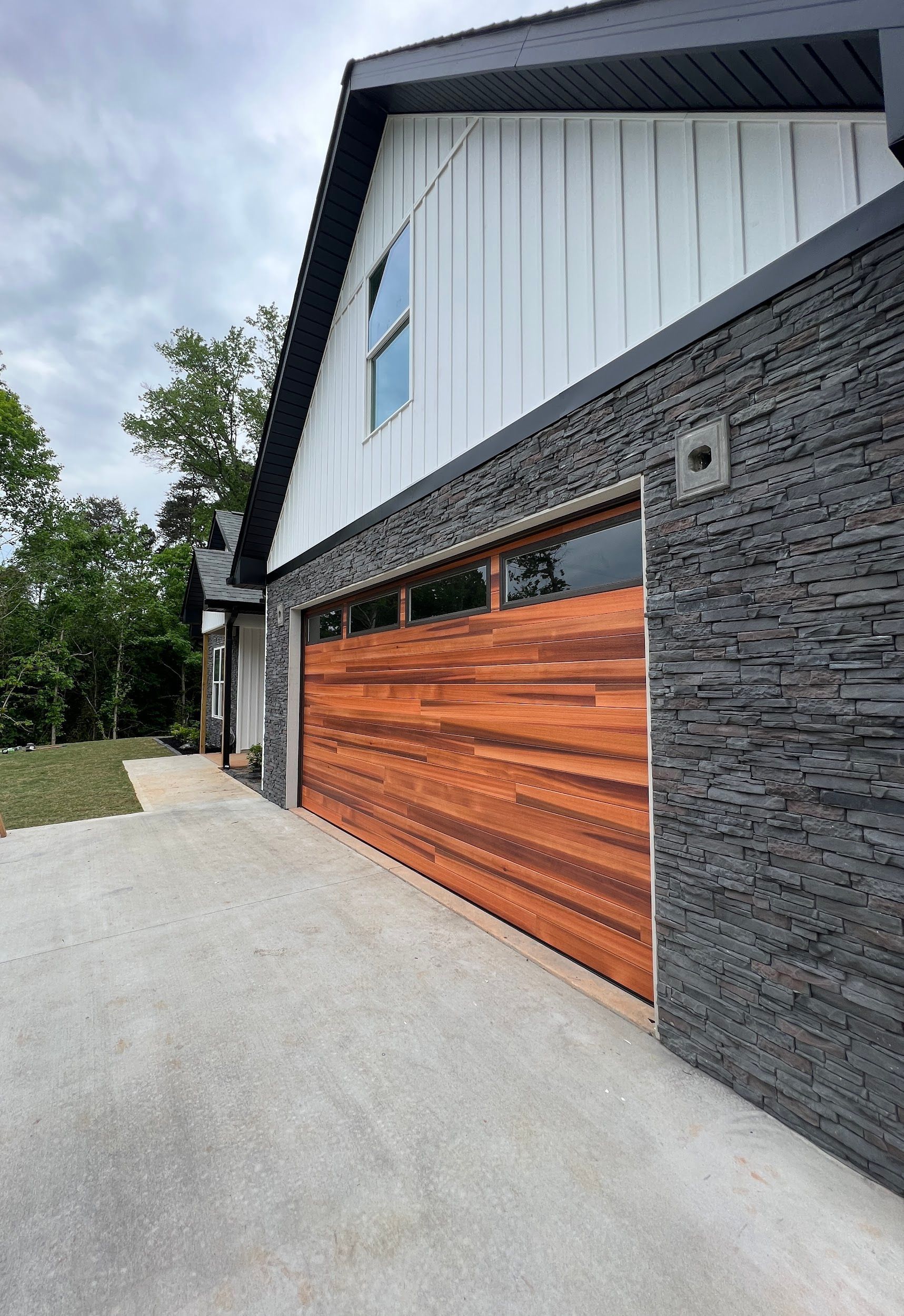 Modern garage with dark stone, cedar door, white siding, and overcast sky.