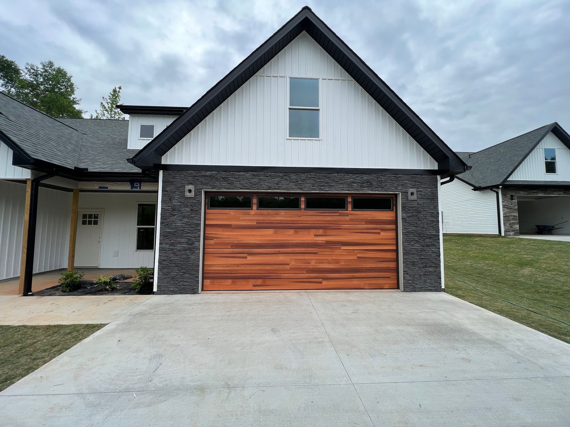 Modern house with brown wooden garage door, gray stonework, and white siding.