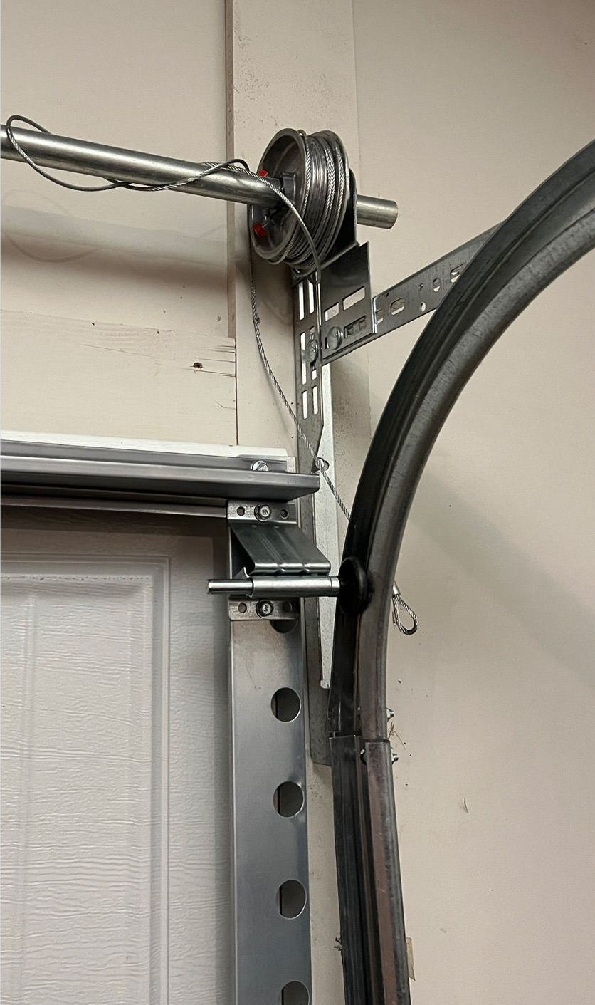 Garage door track with pulley, cable, and support hardware.