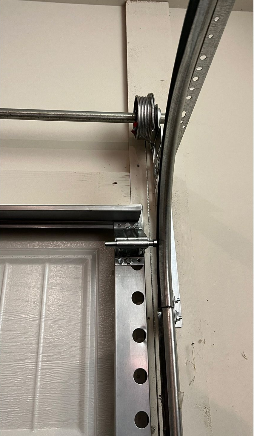 Garage door track with spring and roller assembly mounted on a wall.