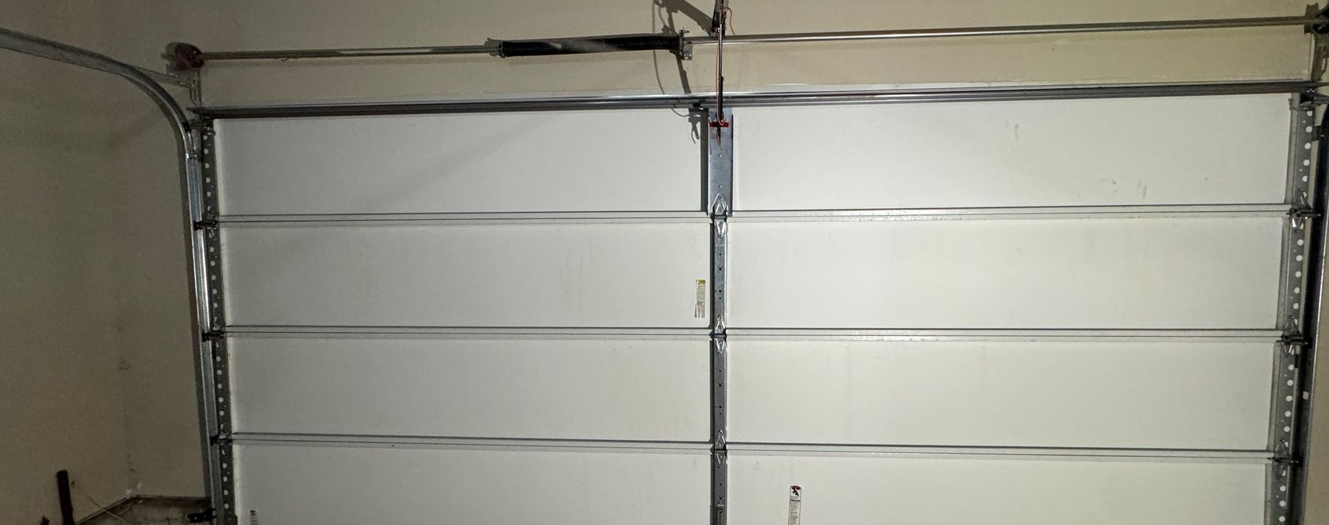 A white closed garage door with horizontal panels and a metal frame.  The door is in an indoor garage setting.