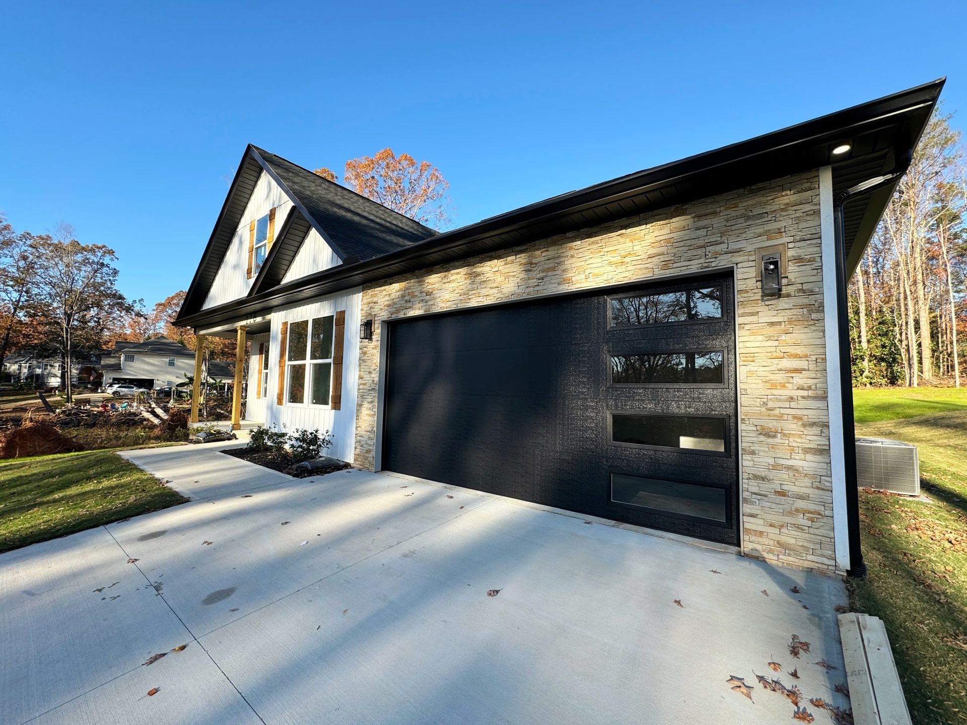 Modern house with black garage door, beige brick facade, white trim, and a concrete driveway on a sunny day.