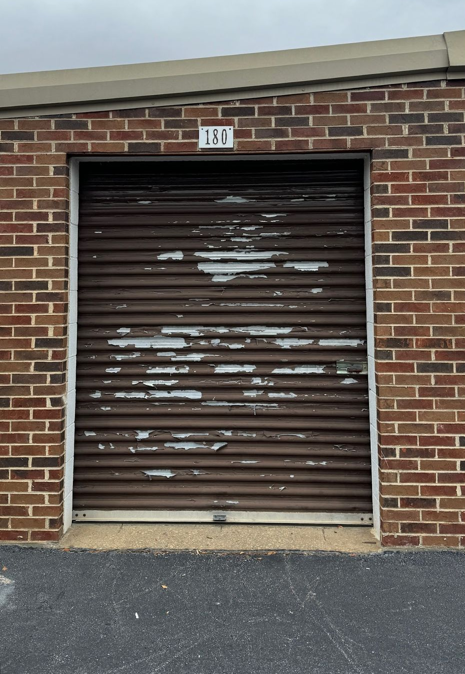 Brown storage unit door with peeling paint set in a brick building.