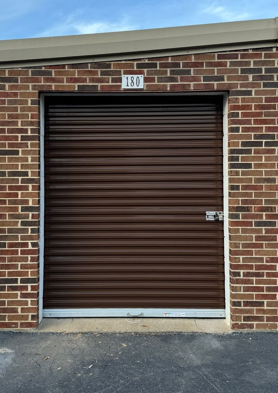 Brown roll-up storage unit door in a brick building. Number 130 above the door.