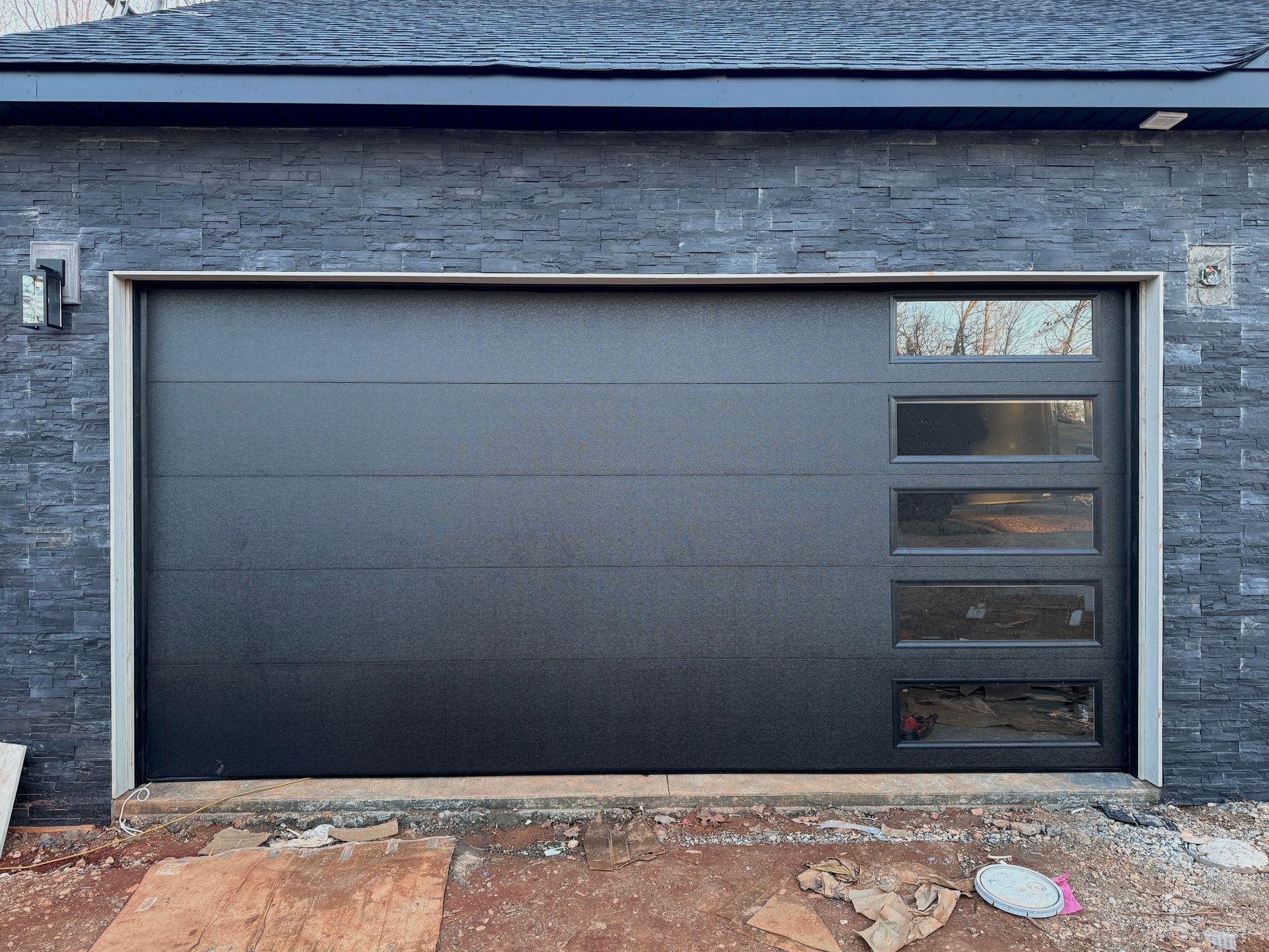 Black garage door with five window panels, set in a grey brick facade.