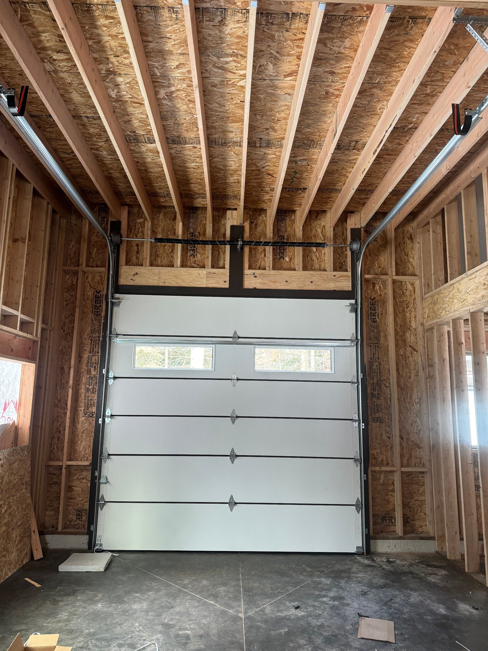 Garage door installed in a wooden framed structure, with visible windows.