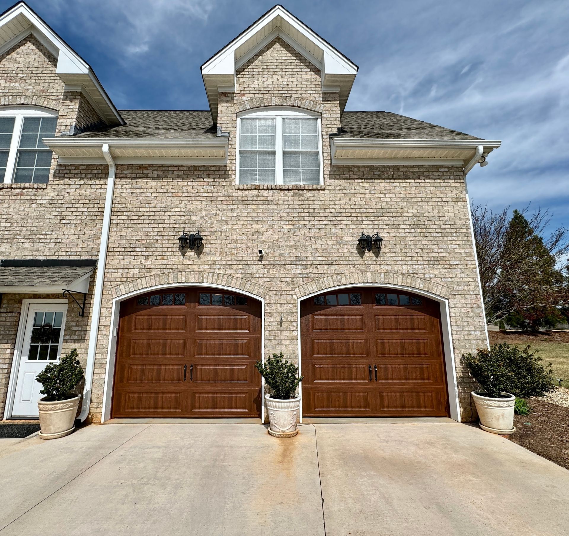 Tan brick townhouse with brown garage doors and a concrete driveway.