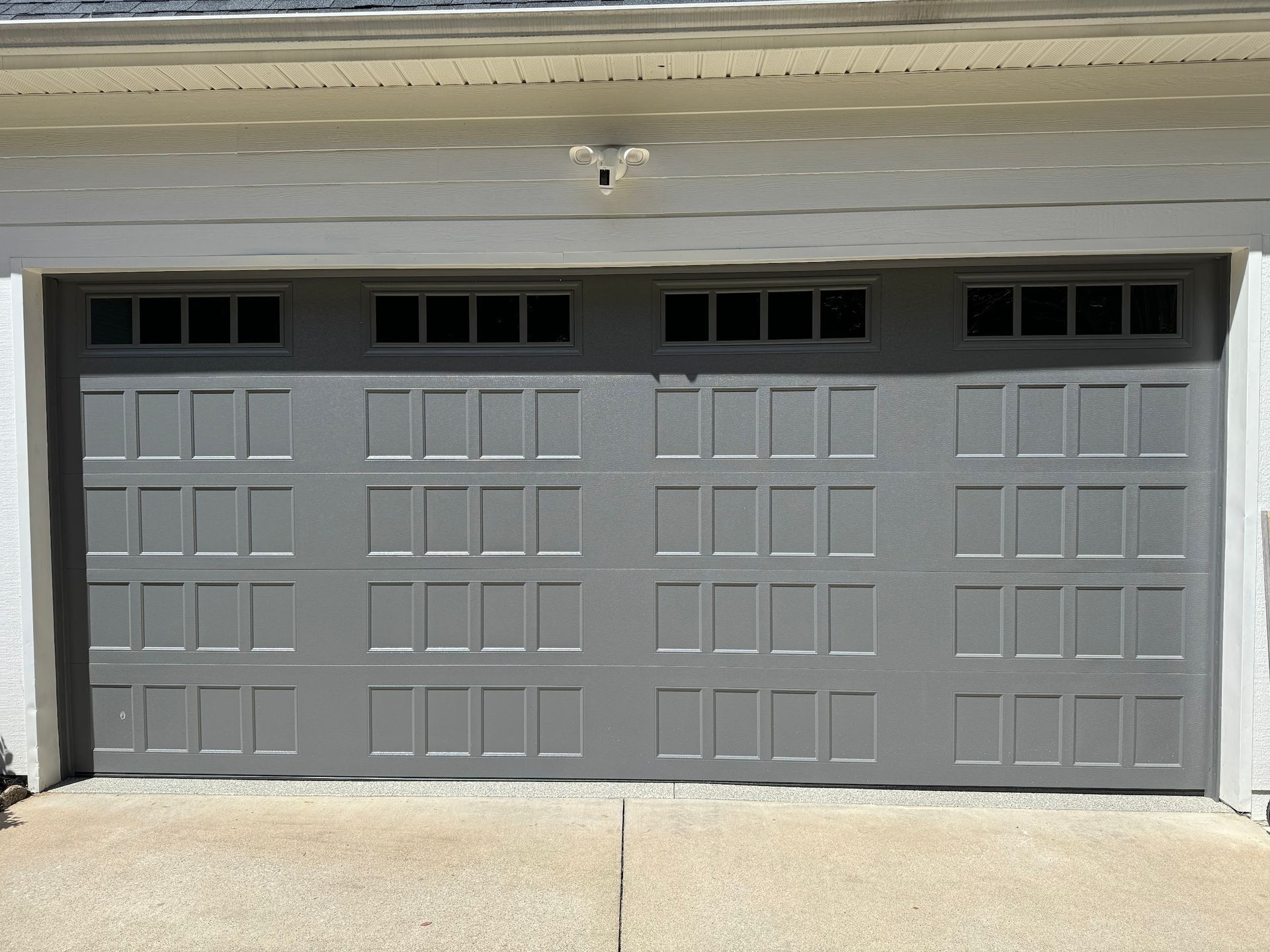 Gray garage door with rectangular windows at the top, on a concrete driveway.