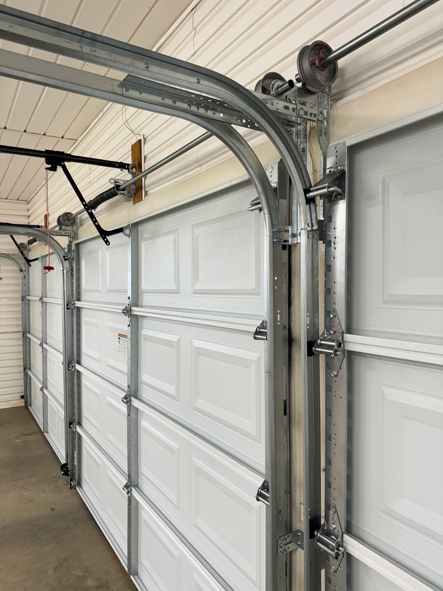 Garage door with white panels and metal tracks curving towards the ceiling.