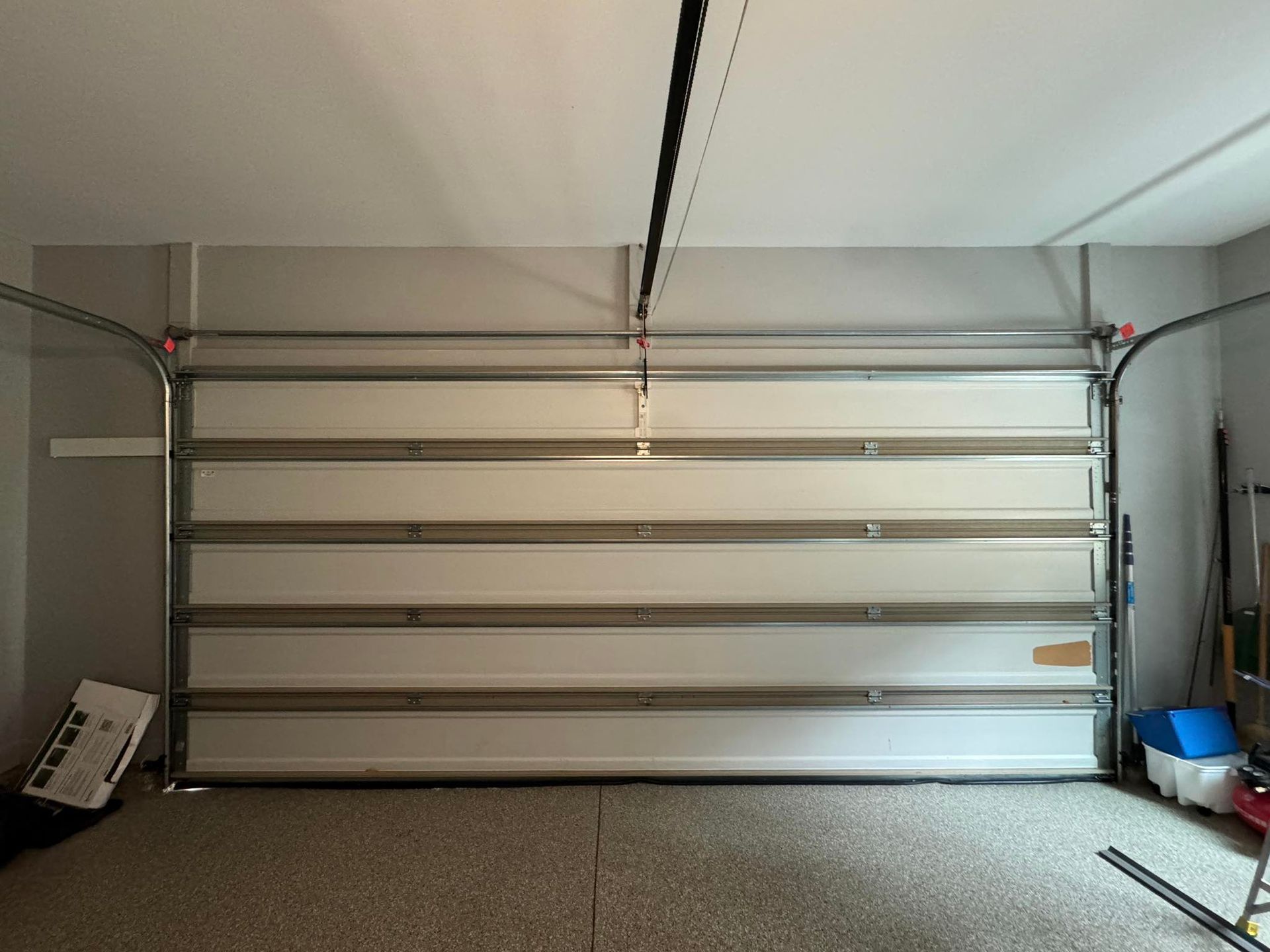 Garage door, closed, with a gray frame, white panels, and a gray garage floor.