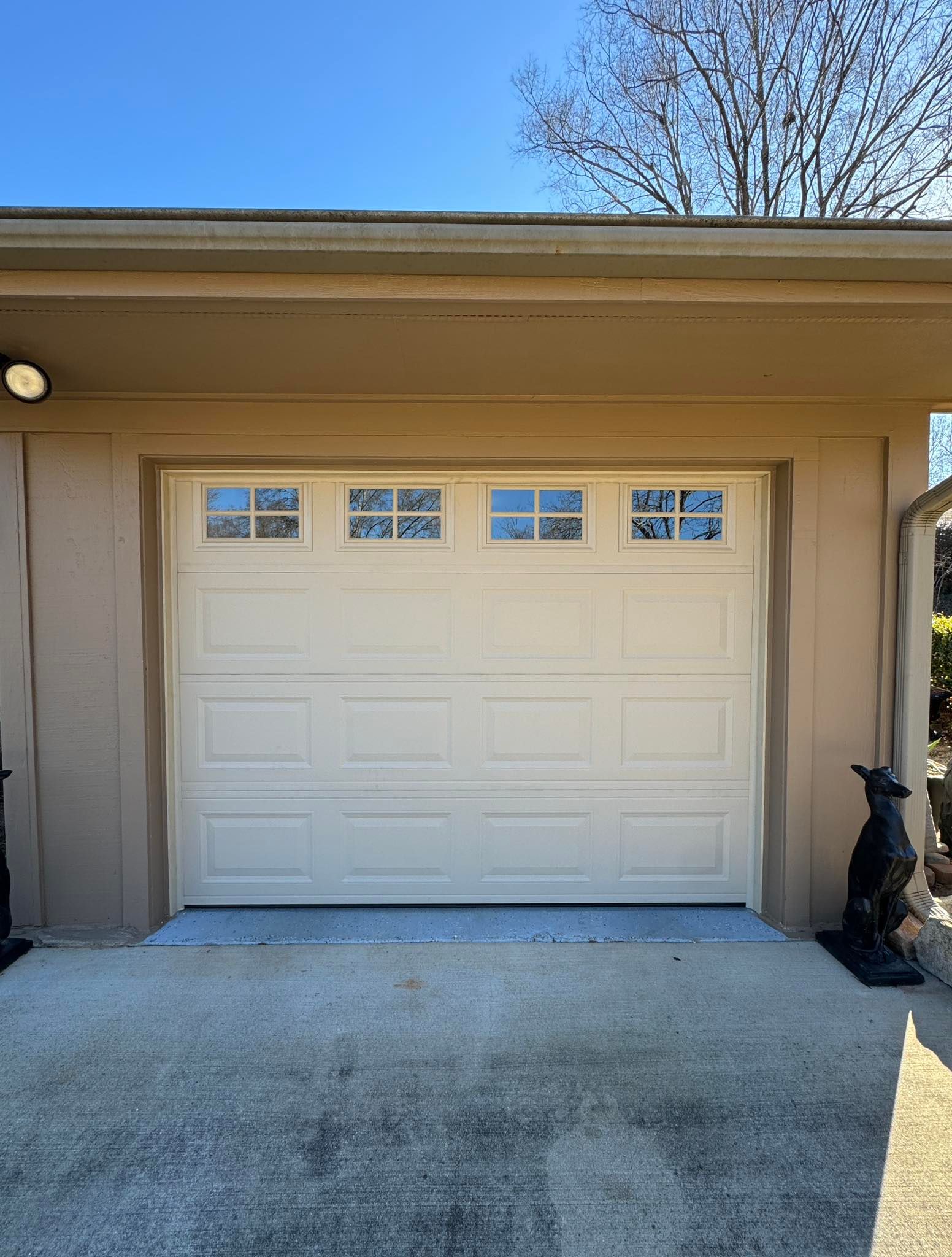 Cream-colored garage door with small windows above, set into a tan building with a concrete driveway.