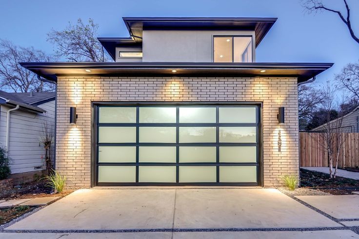 Modern garage with frosted glass door, brick facade, and upper level at dusk.
