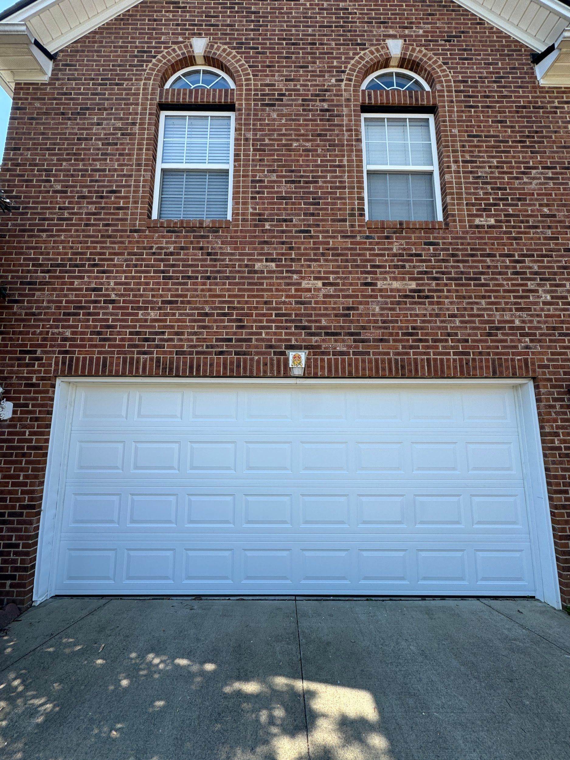 White garage door on a brick house with two arched windows above. Concrete driveway.