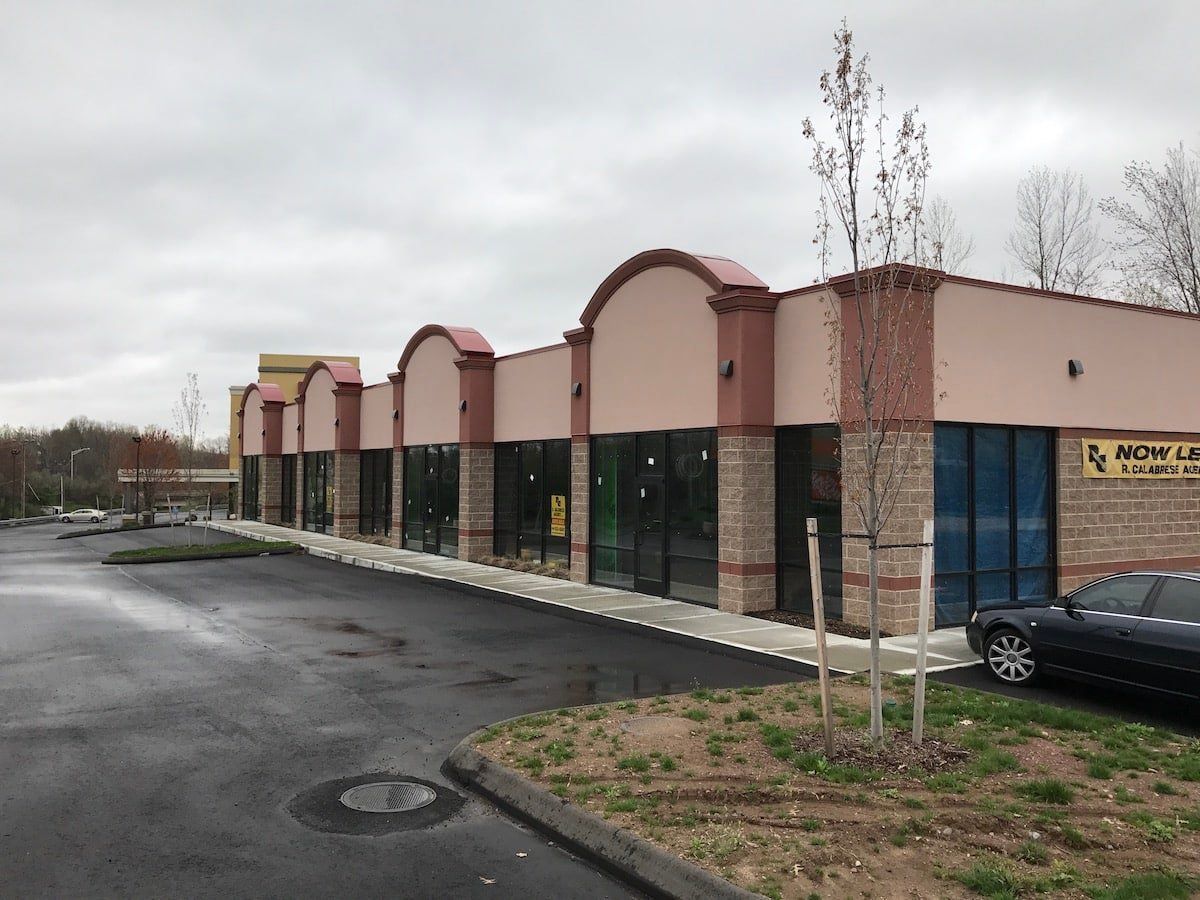 Empty strip mall storefronts on a wet parking lot under an overcast sky