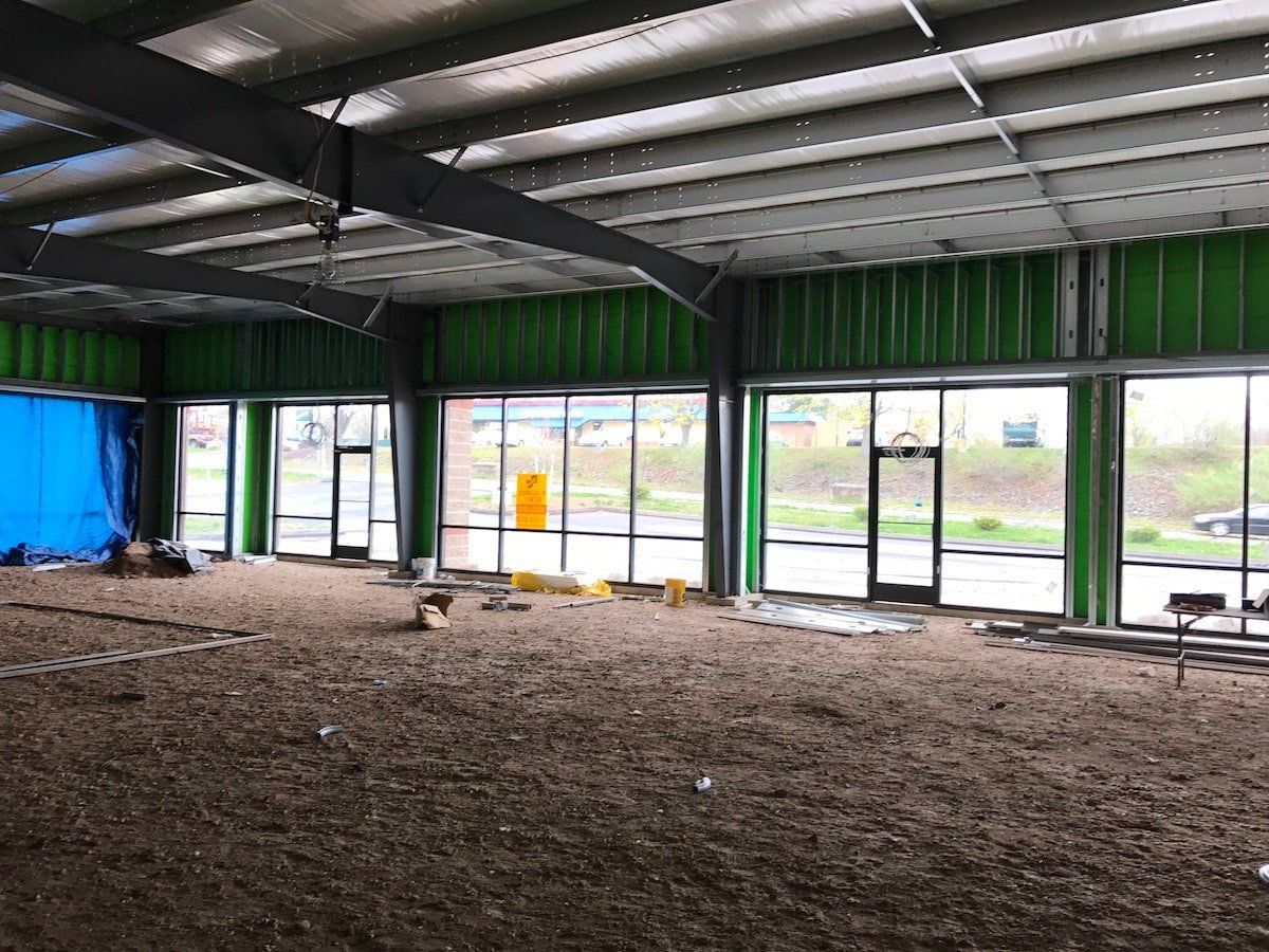 Empty industrial interior with green steel walls, large windows, and gravel floor during construction