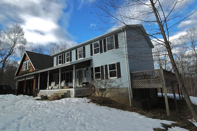 Two-story blue house with porch and snow-covered yard under a cloudy sky
