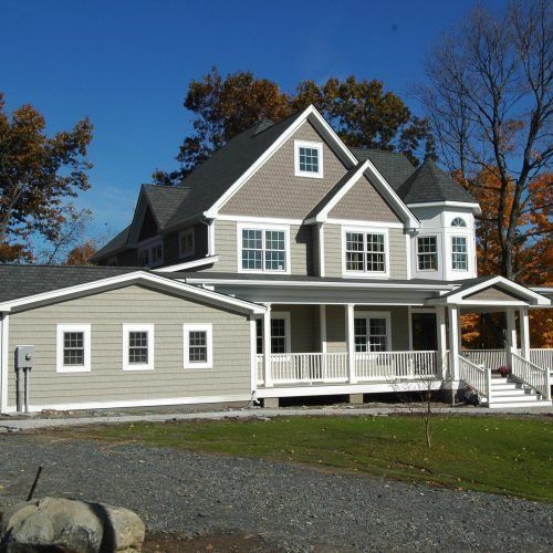 Large gray two-story house with white trim and porch in a sunny suburban yard