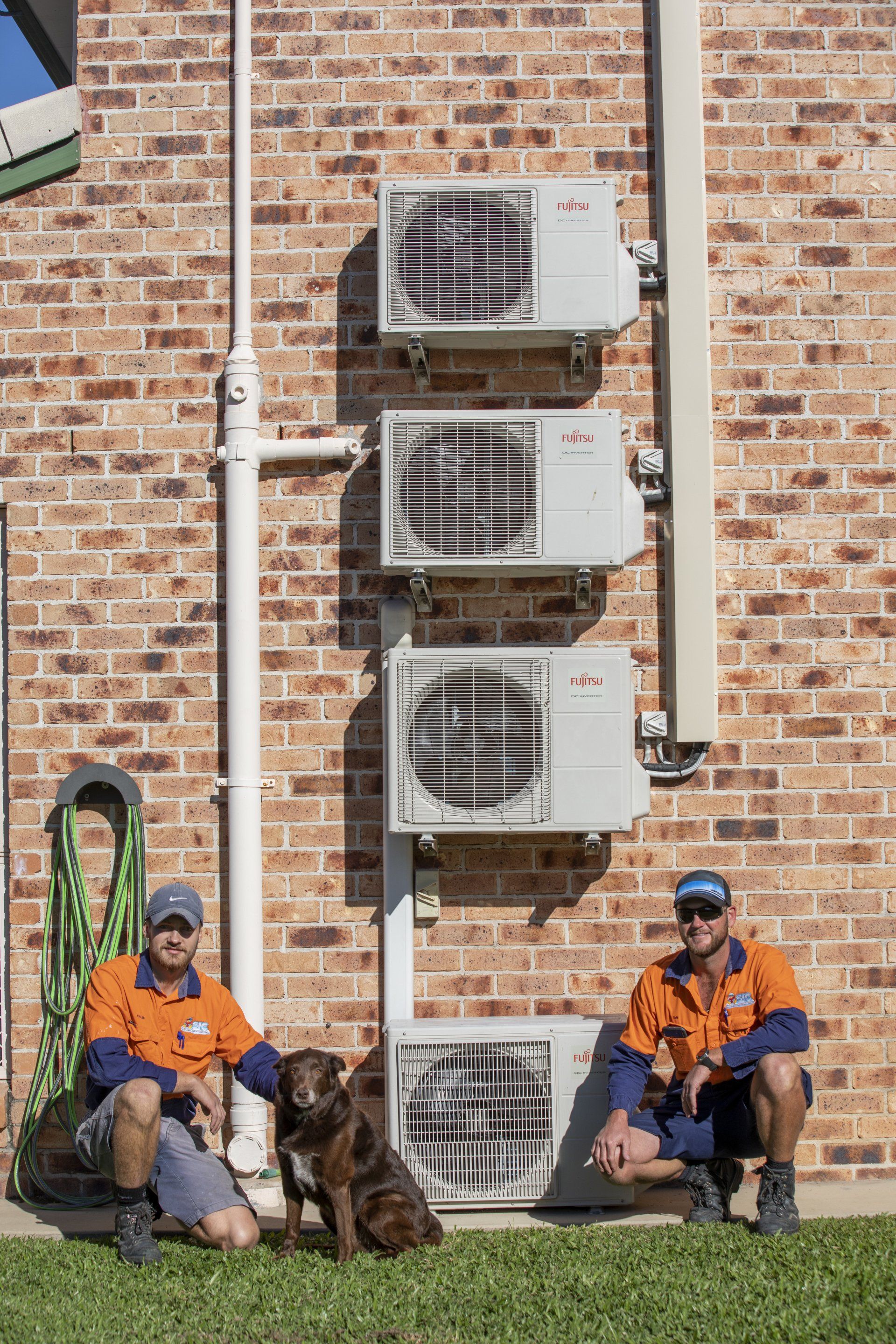 Two men and a dog are Sitting in front of a brick Building - SIC Airconditioning & Refrigeration in Townsville
