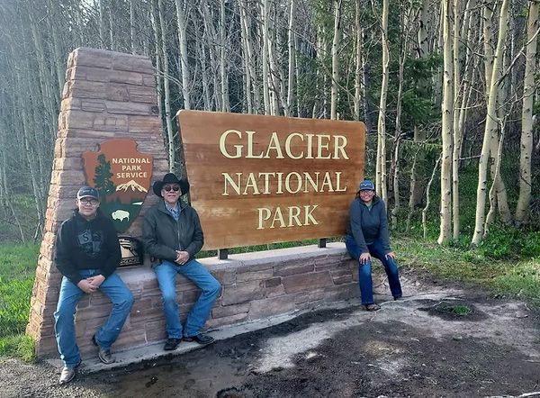 Three Men Are Standing in Front of a Sign That Says Glacier National Park