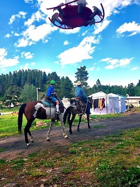 Two People Riding Horses in a Field With a Helicopter in the Background