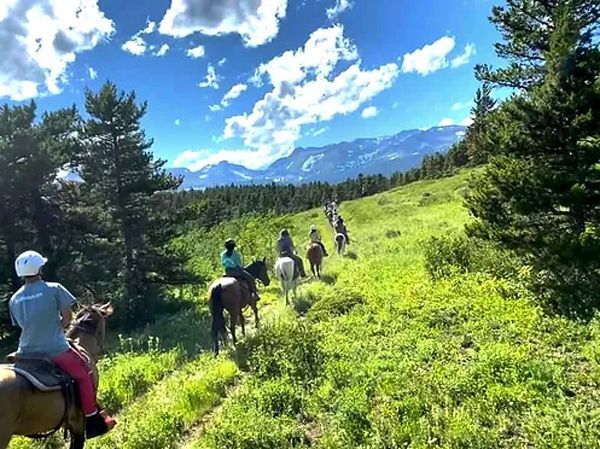 A Group of People Are Riding Horses Down a Grassy Hill