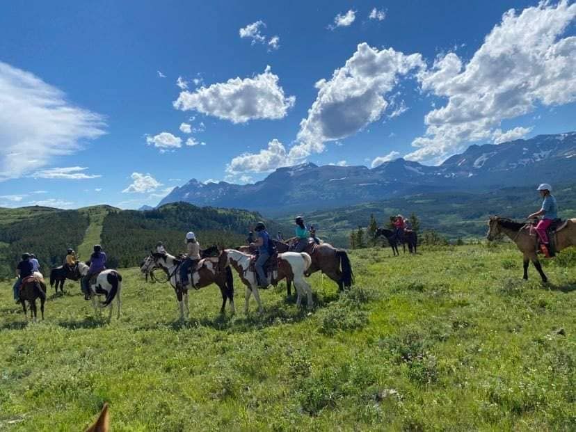 A Group of People Are Riding Horses in a Field With Mountains in the Background