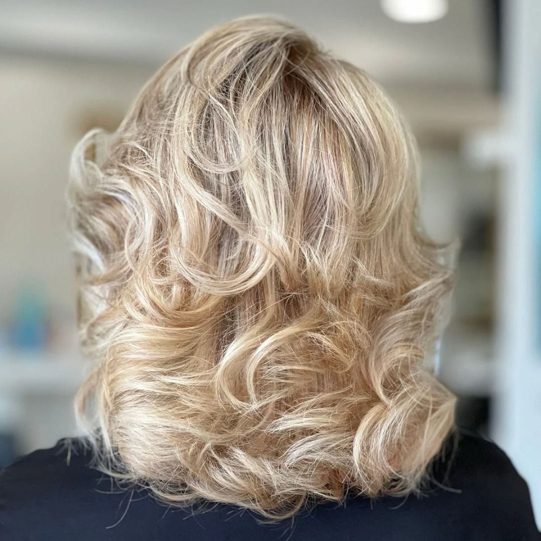 Una vista da dietro di capelli biondi, mossi e lunghi fino alle spalle, con riflessi dorati.