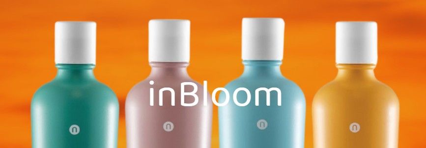 Quattro bottiglie colorate con tappi bianchi, disposte in fila su uno sfondo arancione, con la scritta 