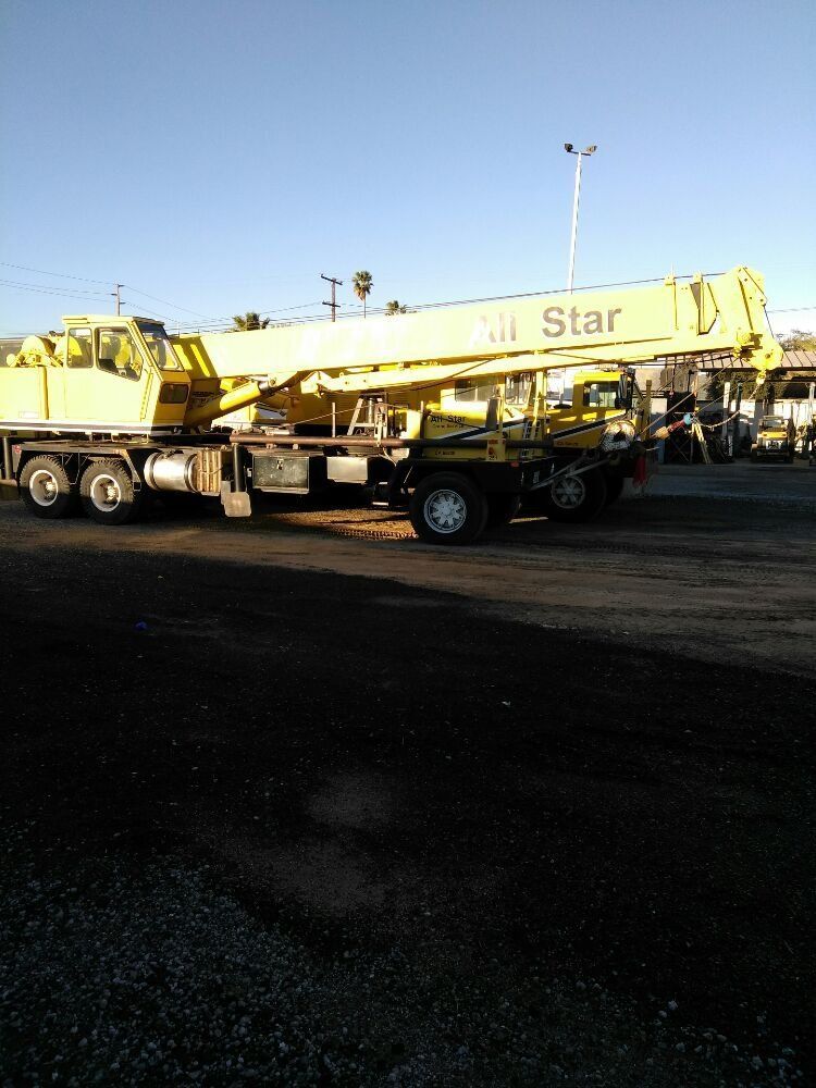 A large yellow crane is parked in a gravel lot.