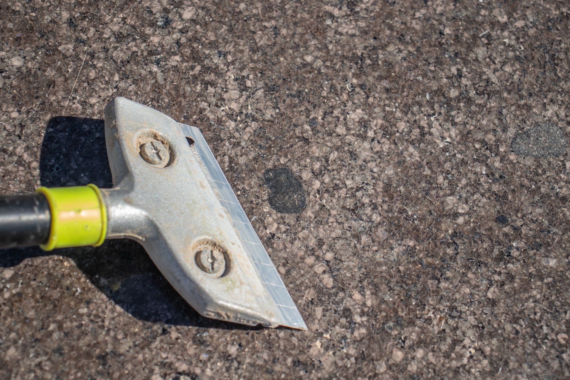 A scraper with a green handle is sitting on a concrete surface.