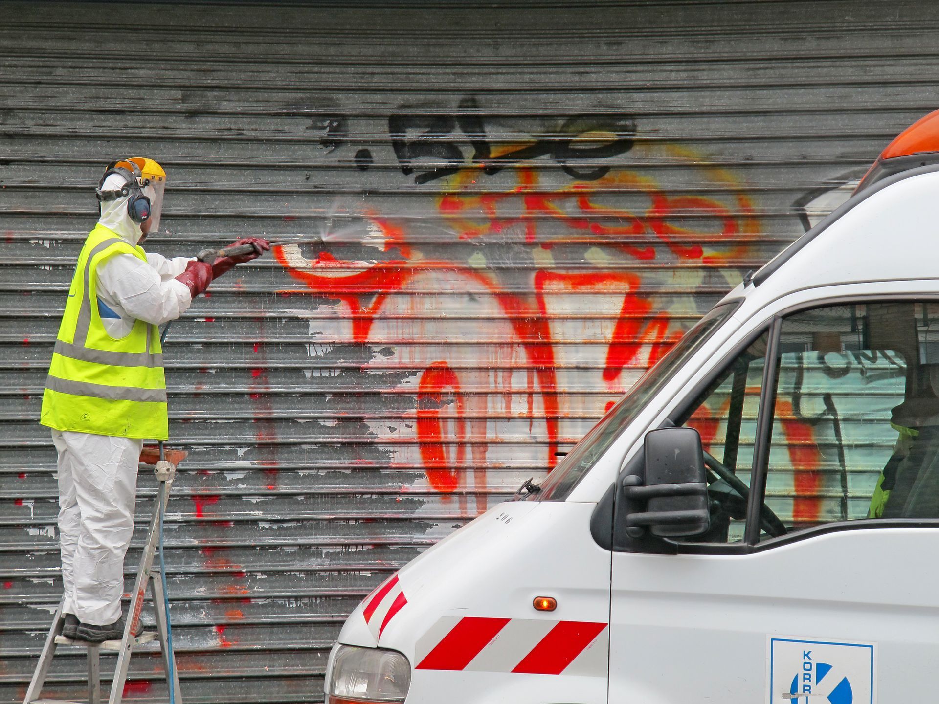 A man is spray painting graffiti on a garage door next to a van.