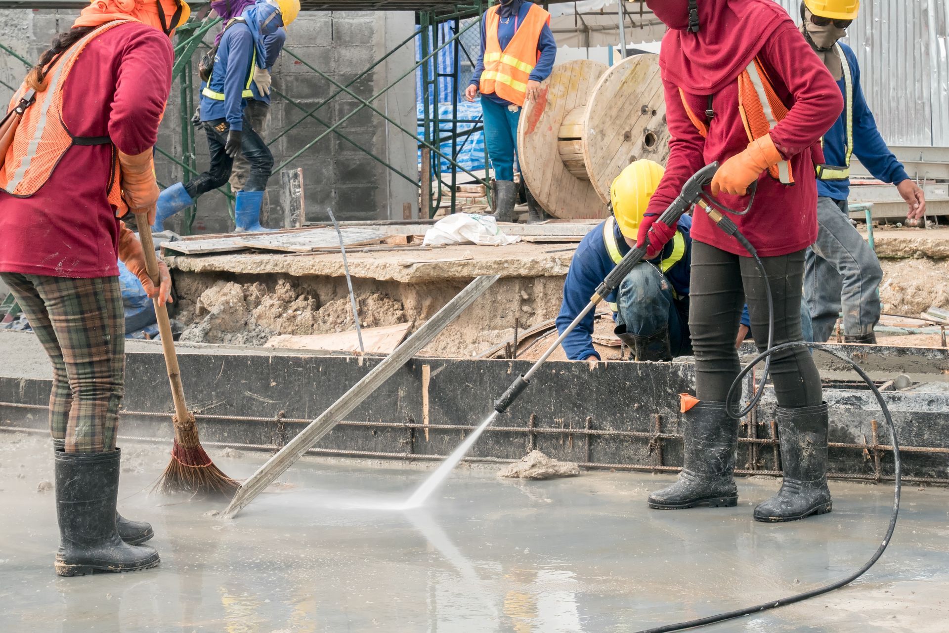 A group of construction workers are cleaning a concrete floor with a high pressure washer.