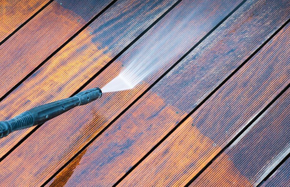 A person is using a high pressure washer to clean a wooden deck.