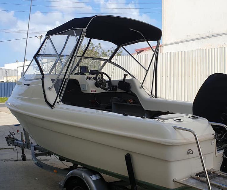 A white motorboat equipped with a black Bimini boat cover, parked outdoors.