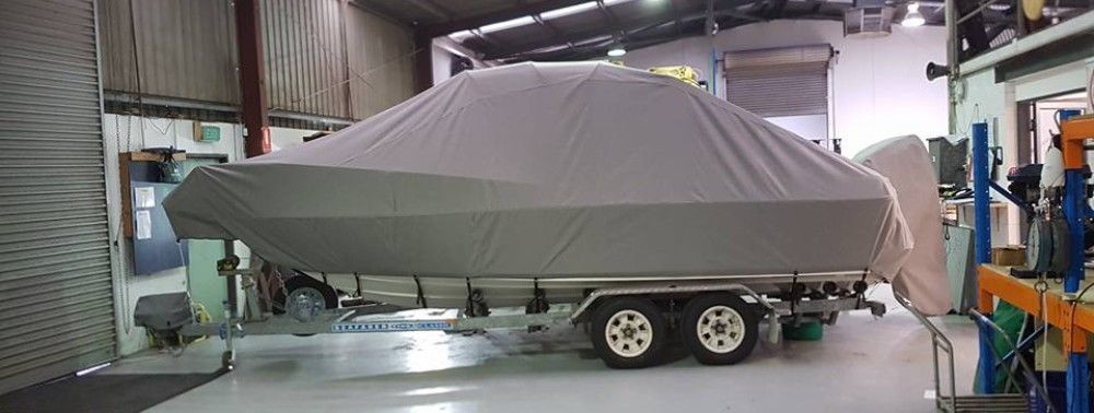 A boat covered with a grey protective cover stored indoors.