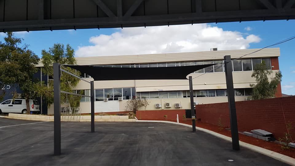Black canvas shade canopy providing cover for a parking area in front of a building