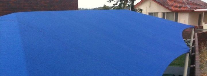 A blue shade sail provides shade and protection for a residential backyard.