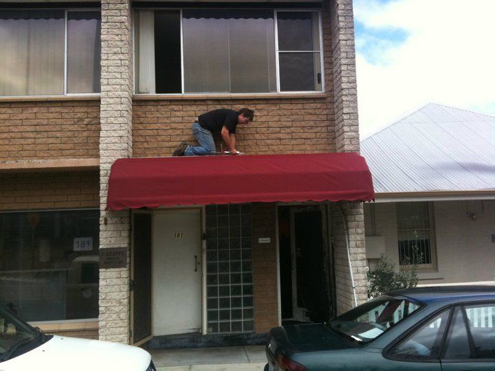 Worker installing a red canvas canopy above the entrance of a commercial building