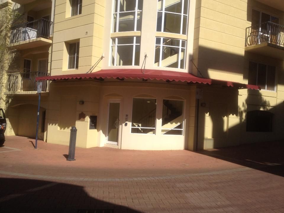 Red canvas canopy awning over apartment building entrance with glass doors and windows