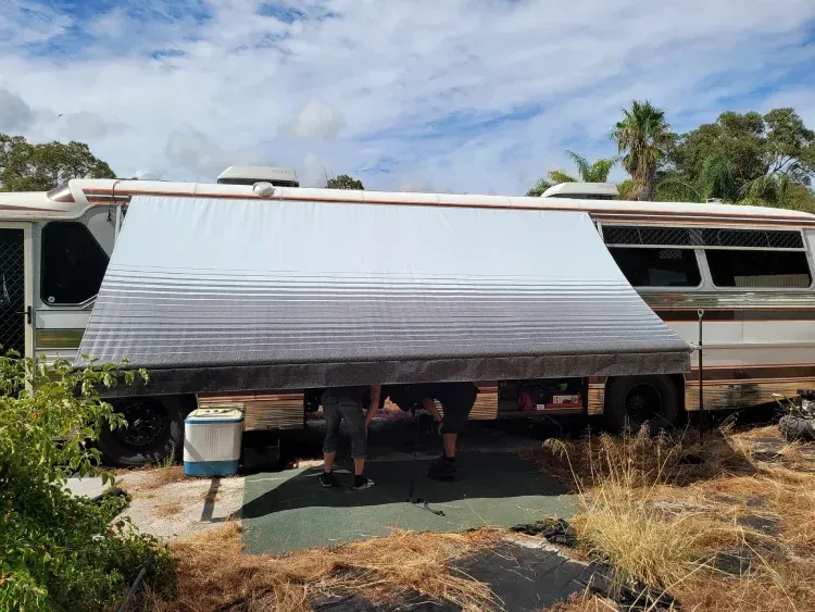 long, gradient-colored awning, fading from light grey to dark grey, extended from a large white and brown motorhome or bus conversion