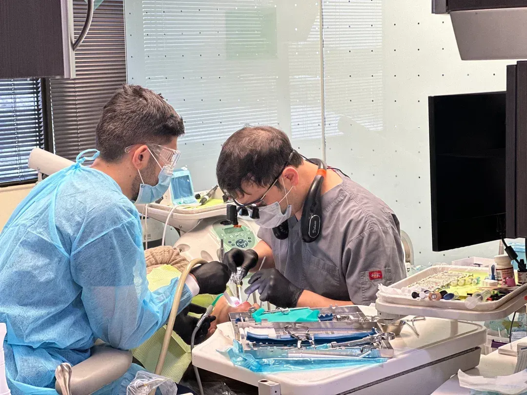 Two dental professionals in surgical attire working on a patient in a dental office.