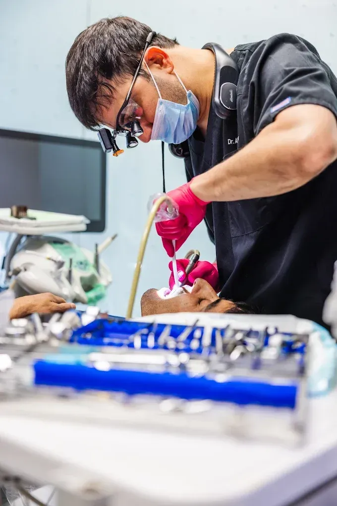 Dentist working on a patient's mouth.  The dentist wears glasses, a mask, and surgical gloves. A dental setting with tools.