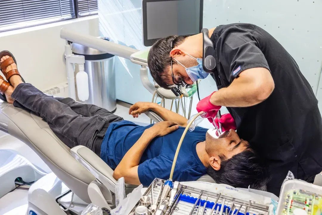 Dentist examining a patient's teeth in a dental chair; medical tools on tray.