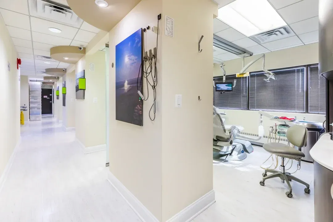 Hallway in a dental office with an open treatment room; light walls, flooring, and dental equipment.