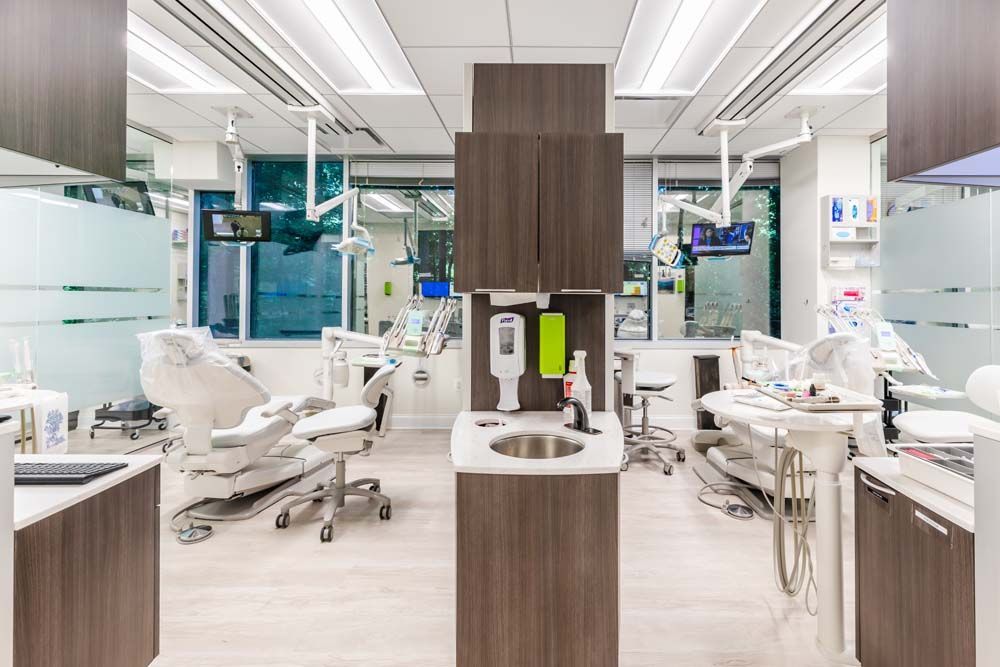 A modern dental clinic with two patient chairs, medical equipment, a central sink, and cabinets in a bright, open layout.