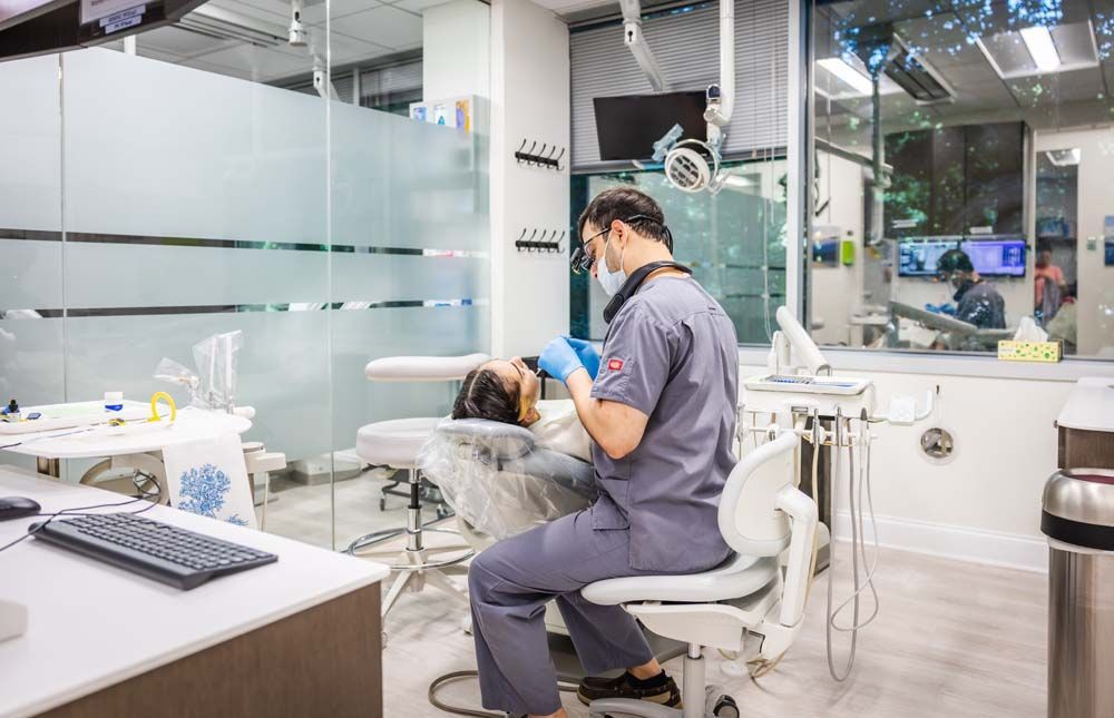 Dentist examining a patient in a dental office; doctor wears scrubs and mask.