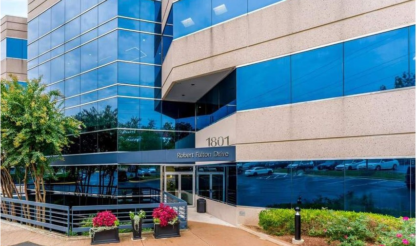 Brick office building with curved corner, fountain, and parked cars under a blue sky.