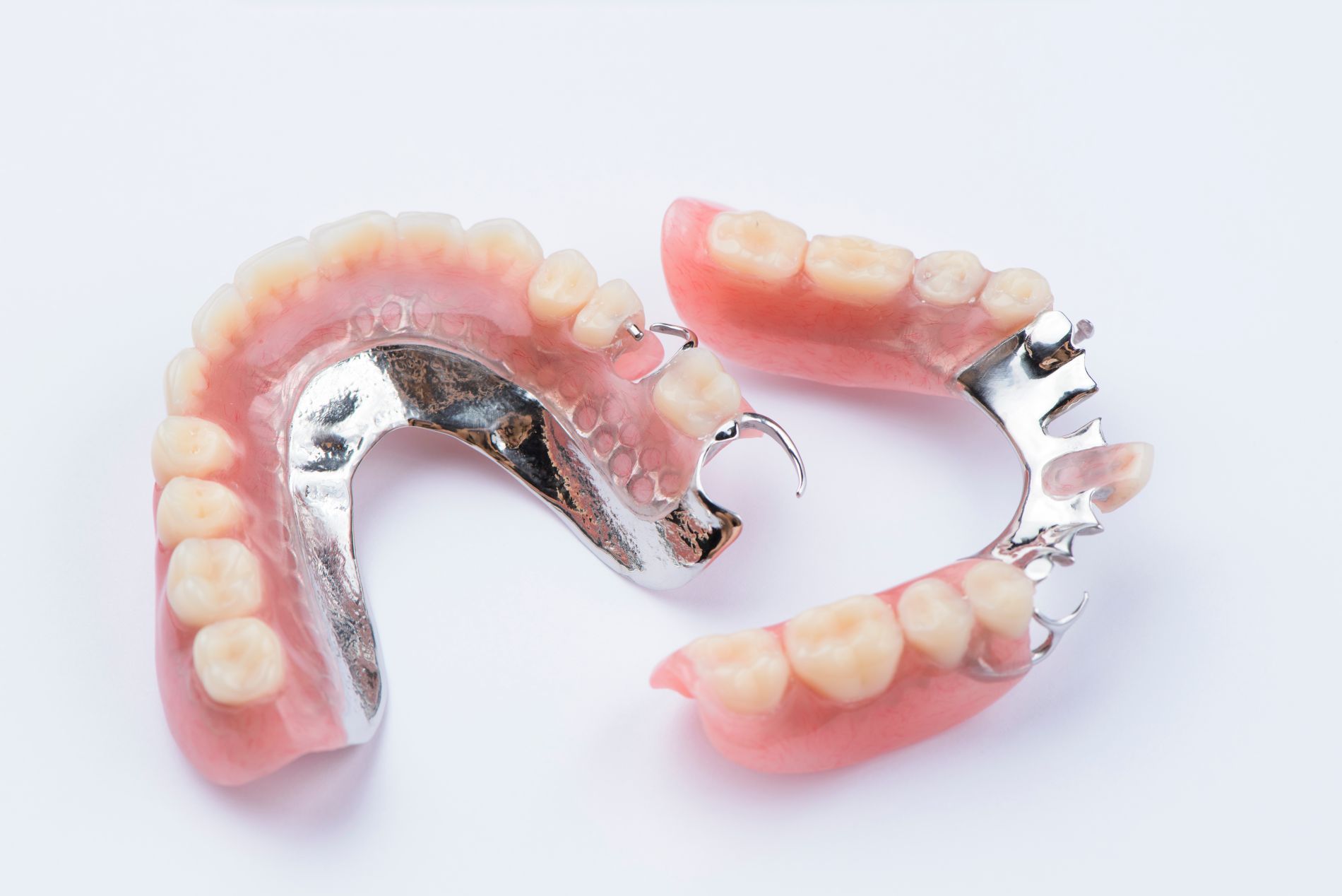 Partial dentures, pink gum and white teeth, with metal clasps, set against a white background.