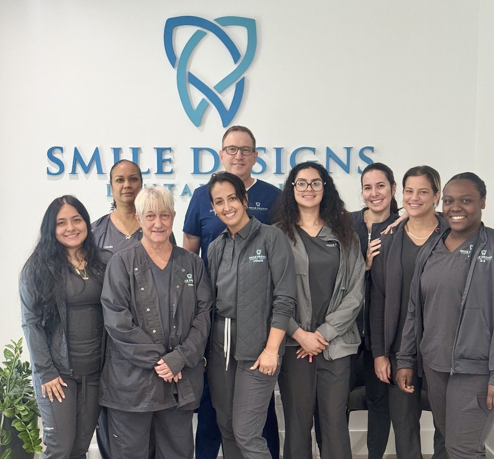 Smile Designs Dental staff posing together in front of their office sign.